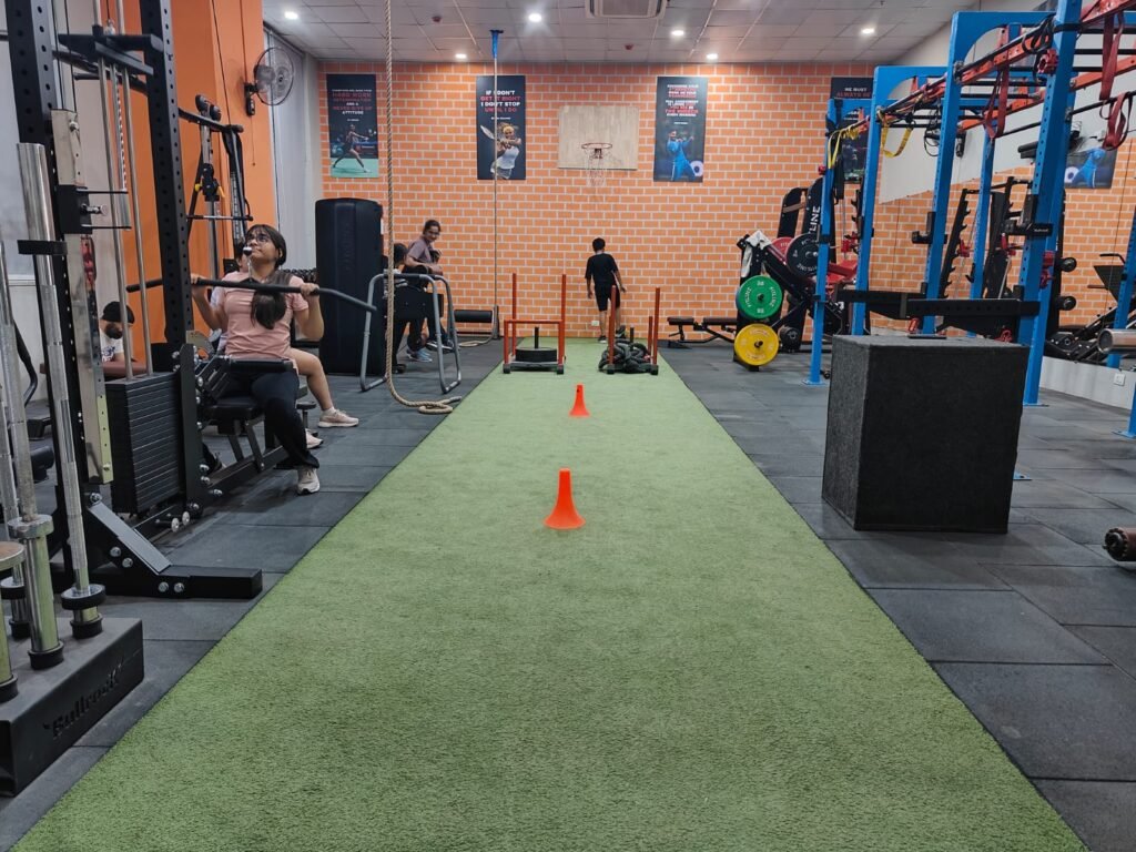 Members training at BMilitaryFit Noida studio on turf track with strength machines, ropes and functional equipment.