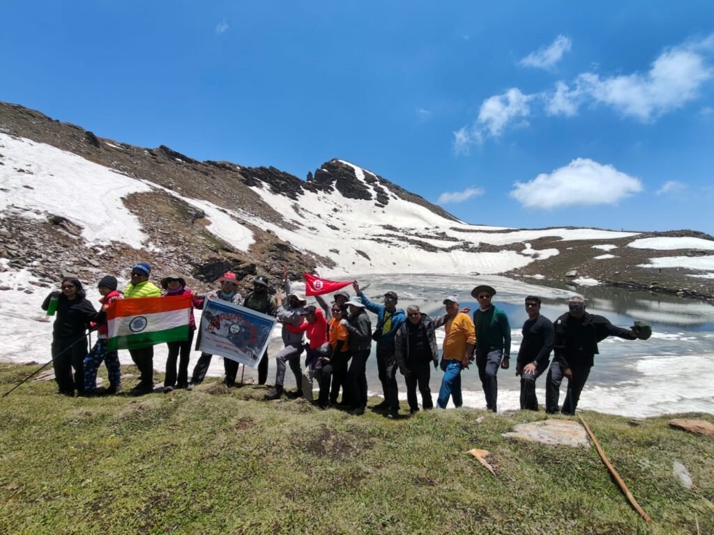 BMilitaryFit Noida members on a high-altitude trek posing with flags beside a snow-lined lake and mountain backdrop.