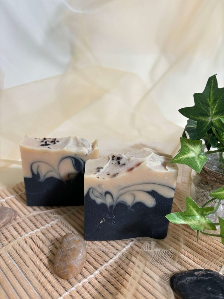 Two Rungli Rungliot handcrafted soap bars in black and cream swirls styled with stones and ivy