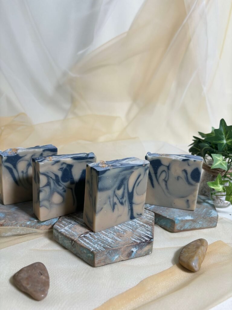 Handmade artisan soap bars with blue swirls by Rungli Rungliot displayed on rustic wooden blocks