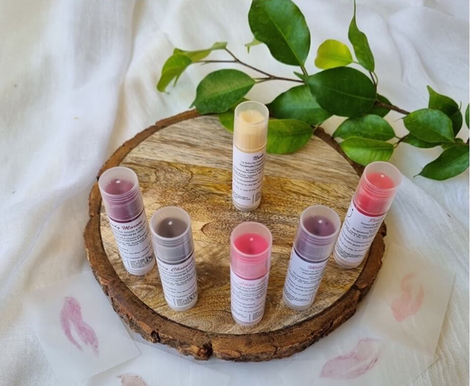 Rungli Rungliot tinted lip balms in multiple shades arranged on a wooden slice with green leaves and lip swatches