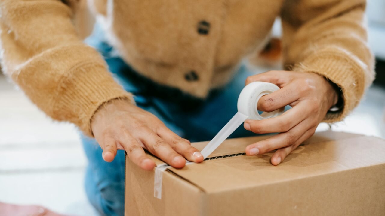 Worker sealing a cardboard box in a warehouse, logistics hub, supply chain.