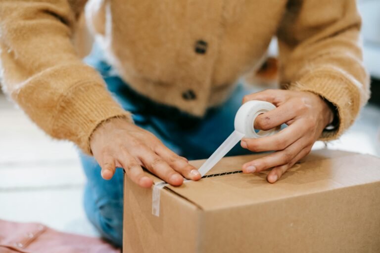 Worker sealing a cardboard box in a warehouse, logistics hub, supply chain.