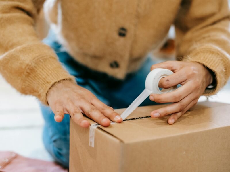 Worker sealing a cardboard box in a warehouse, logistics hub, supply chain.