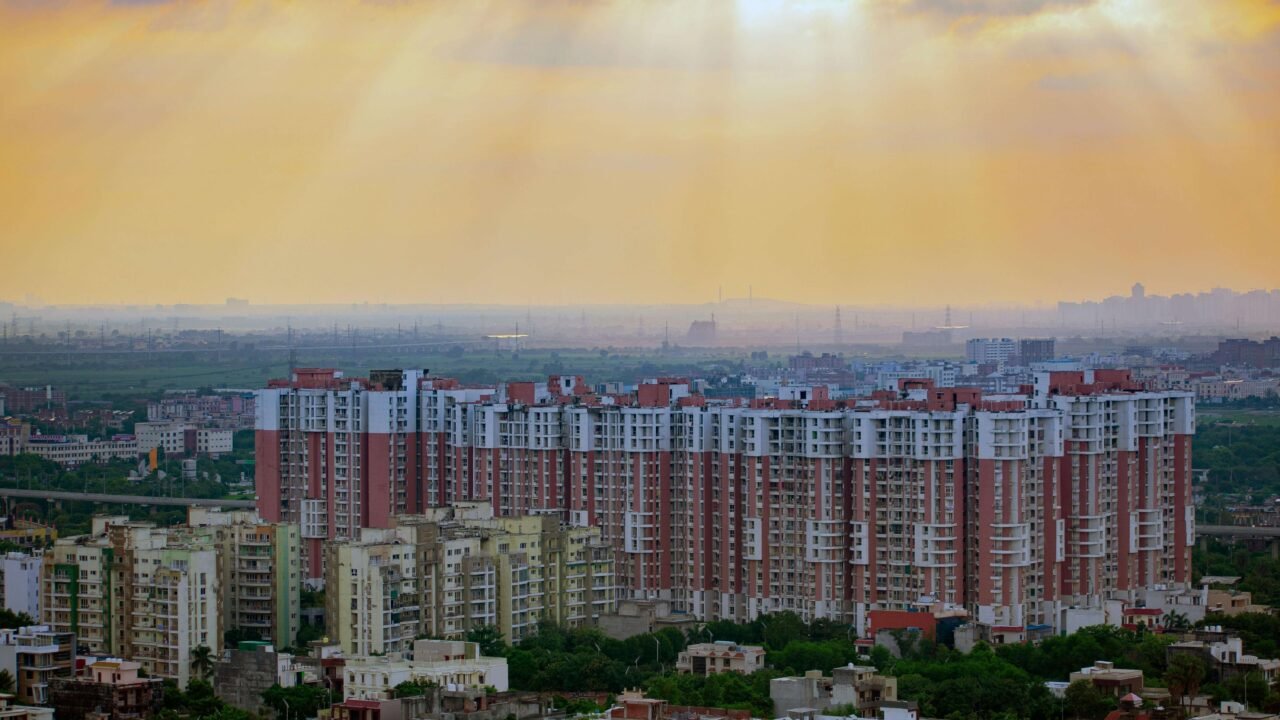 Aerial sunrise view of Noida city with modern high-rise apartments, green neighborhoods, and dramatic sky—symbolizing infrastructure growth and urban development.