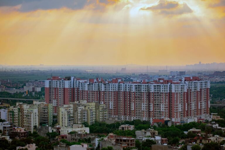 Aerial sunrise view of Noida city with modern high-rise apartments, green neighborhoods, and dramatic sky—symbolizing infrastructure growth and urban development.