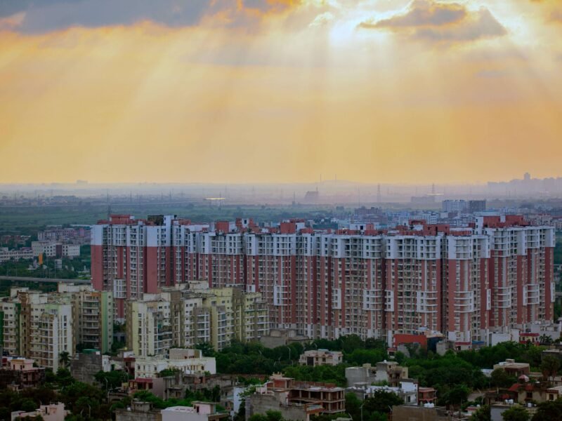 Aerial sunrise view of Noida city with modern high-rise apartments, green neighborhoods, and dramatic sky—symbolizing infrastructure growth and urban development.