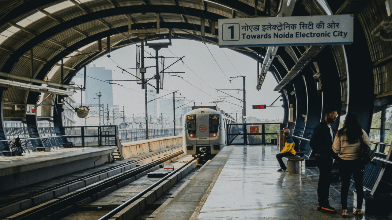 Metro train arriving at a covered station towards Noida Electronic City