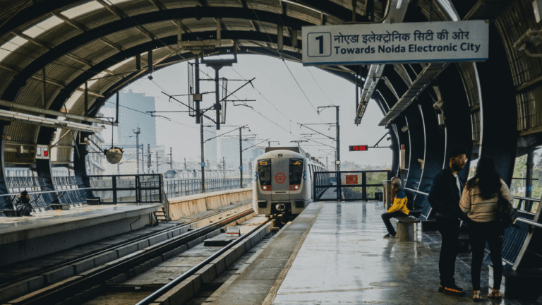 Metro train arriving at a covered station towards Noida Electronic City