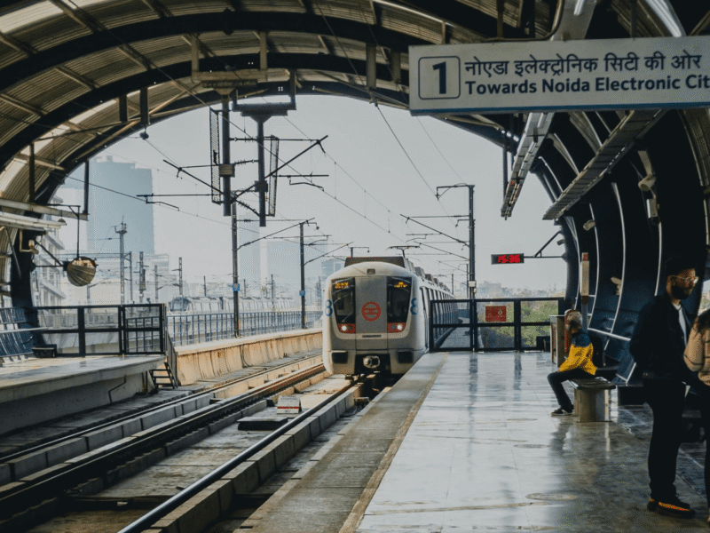 Metro train arriving at a covered station towards Noida Electronic City